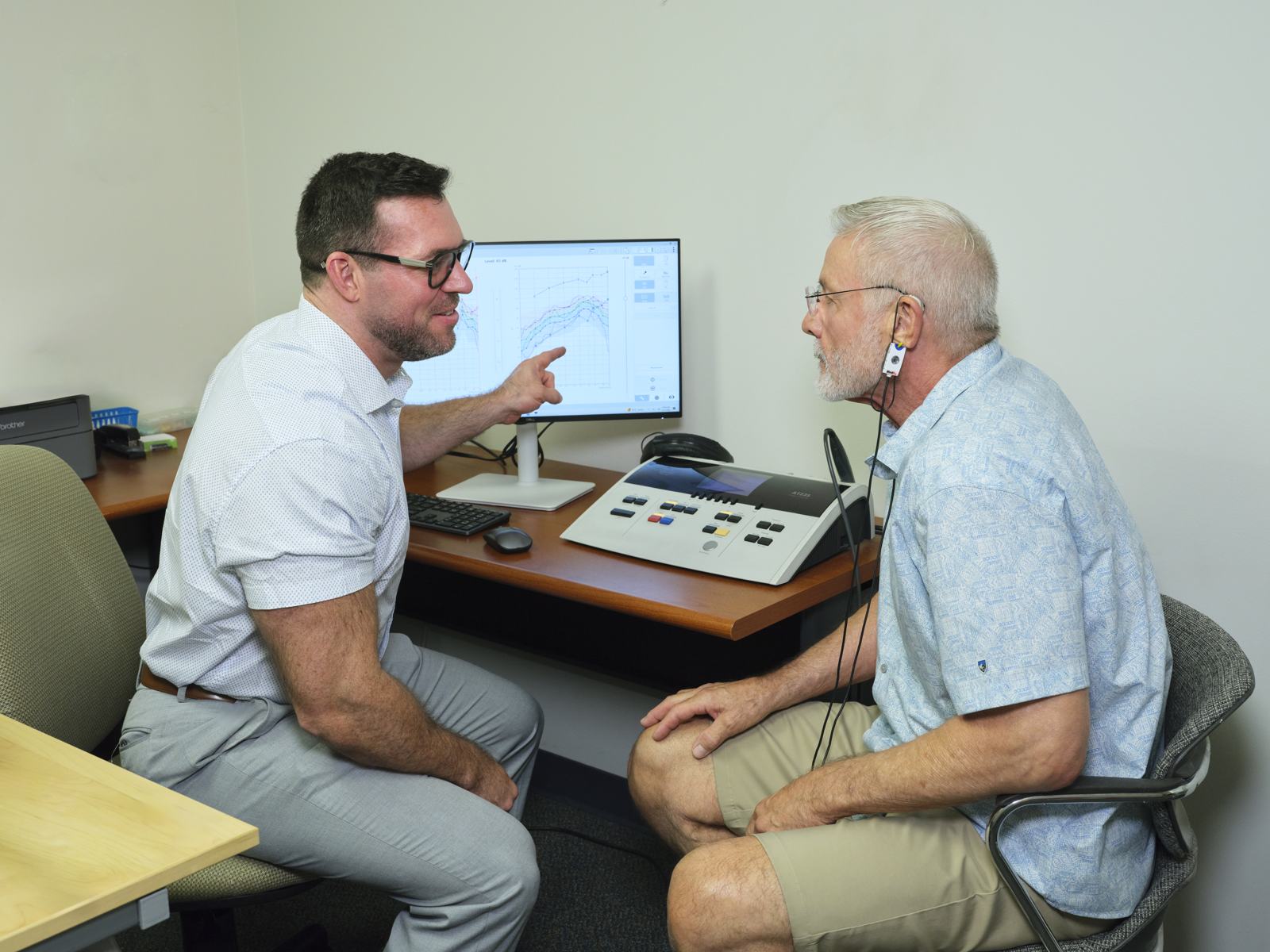 Andy Schirmer pointing at the Real Ear Measurement results on the screen while a patient wearing the probe microphone looks on